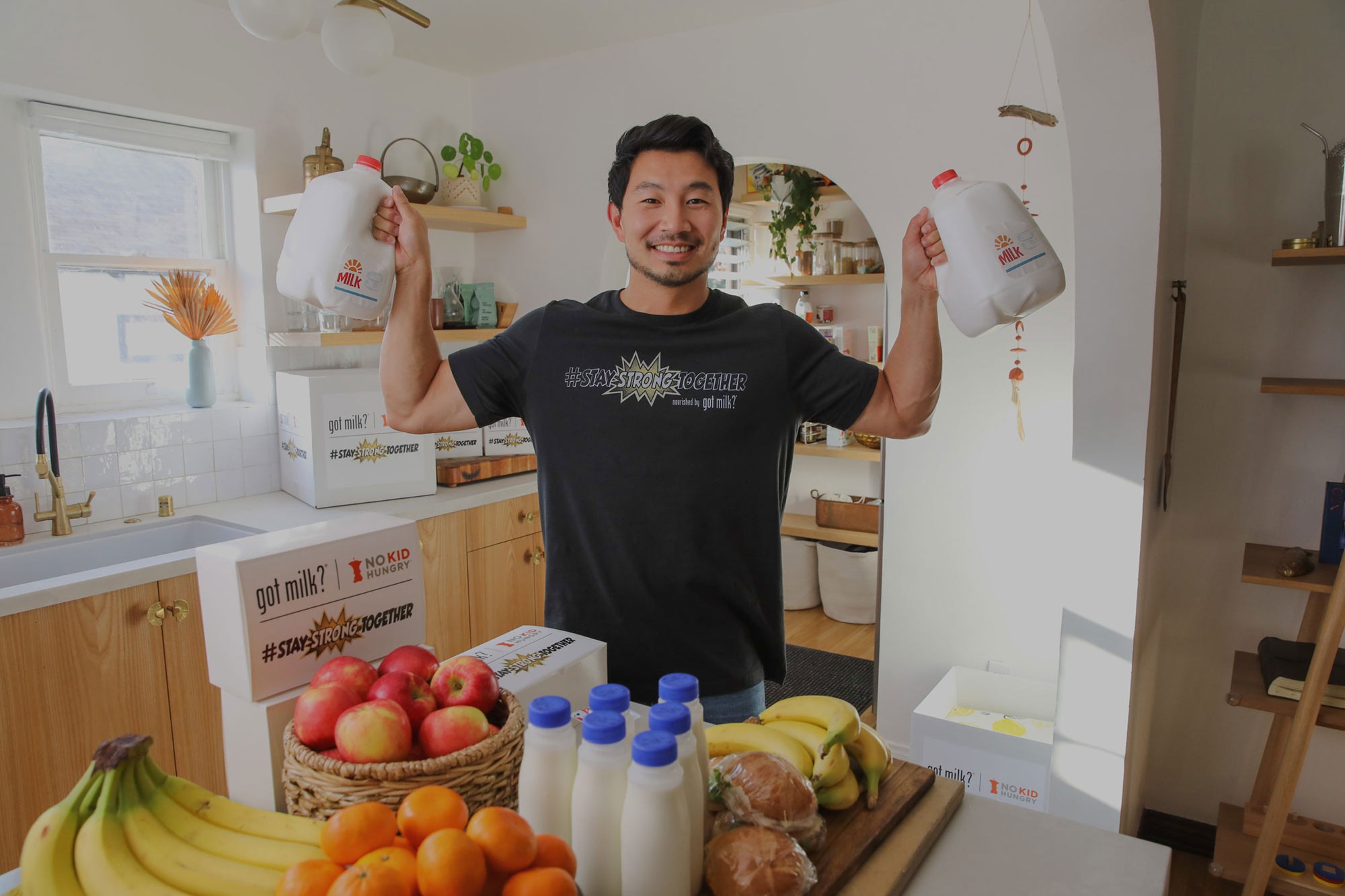 Simu Liu lifting two gallons of milk; the boxes read “got milk? | NO KID HUNGRY #STAY STRONG TOGETHER”