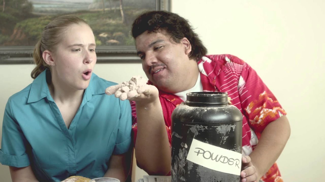 “Milk vs Protein Powder”: a young woman and a man with a tub labelled “POWDER” in a diner booth